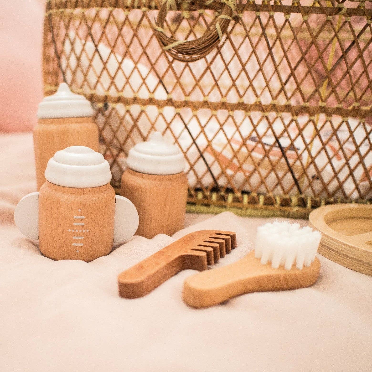 Wooden baby care products including bottles, brush, and comb on a soft surface with a woven basket in the background.