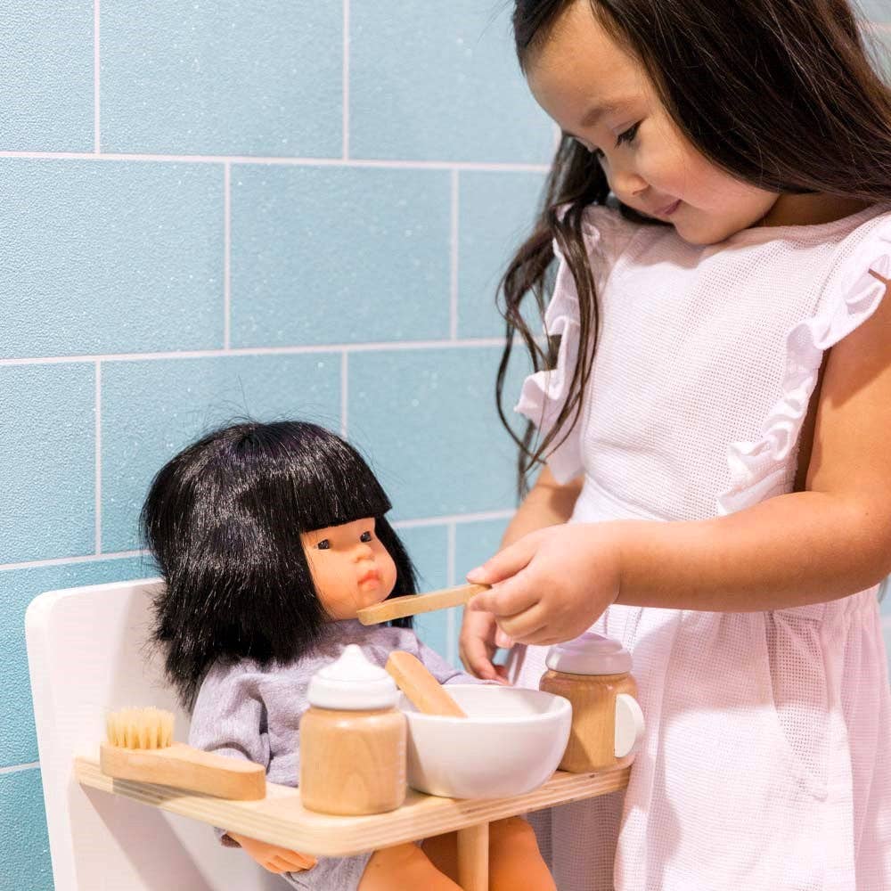 Child using wooden doll accessories to pretend play feeding